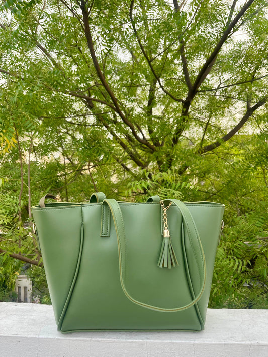Graciza green faux leather Aura tote bag with gold-tone hardware and decorative tassel, set against a leafy backdrop.
