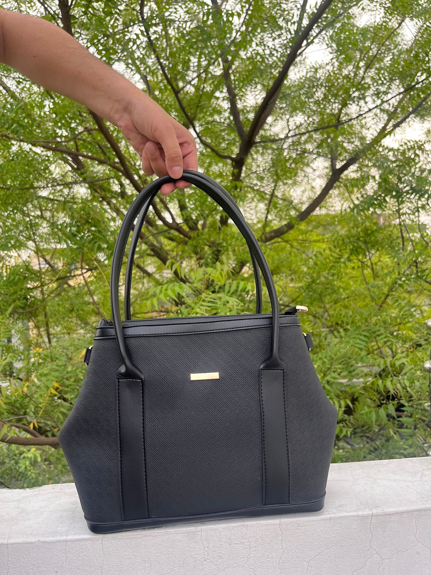 Graciza black faux leather Aero shoulder bag with flared wing design, gold bar hardware, and structured silhouette.