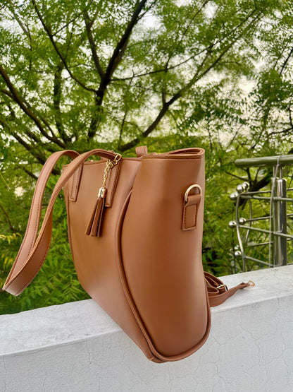 Graciza Aura brown faux leather tote bag with gold hardware, tassel detail, and double handles outdoors.