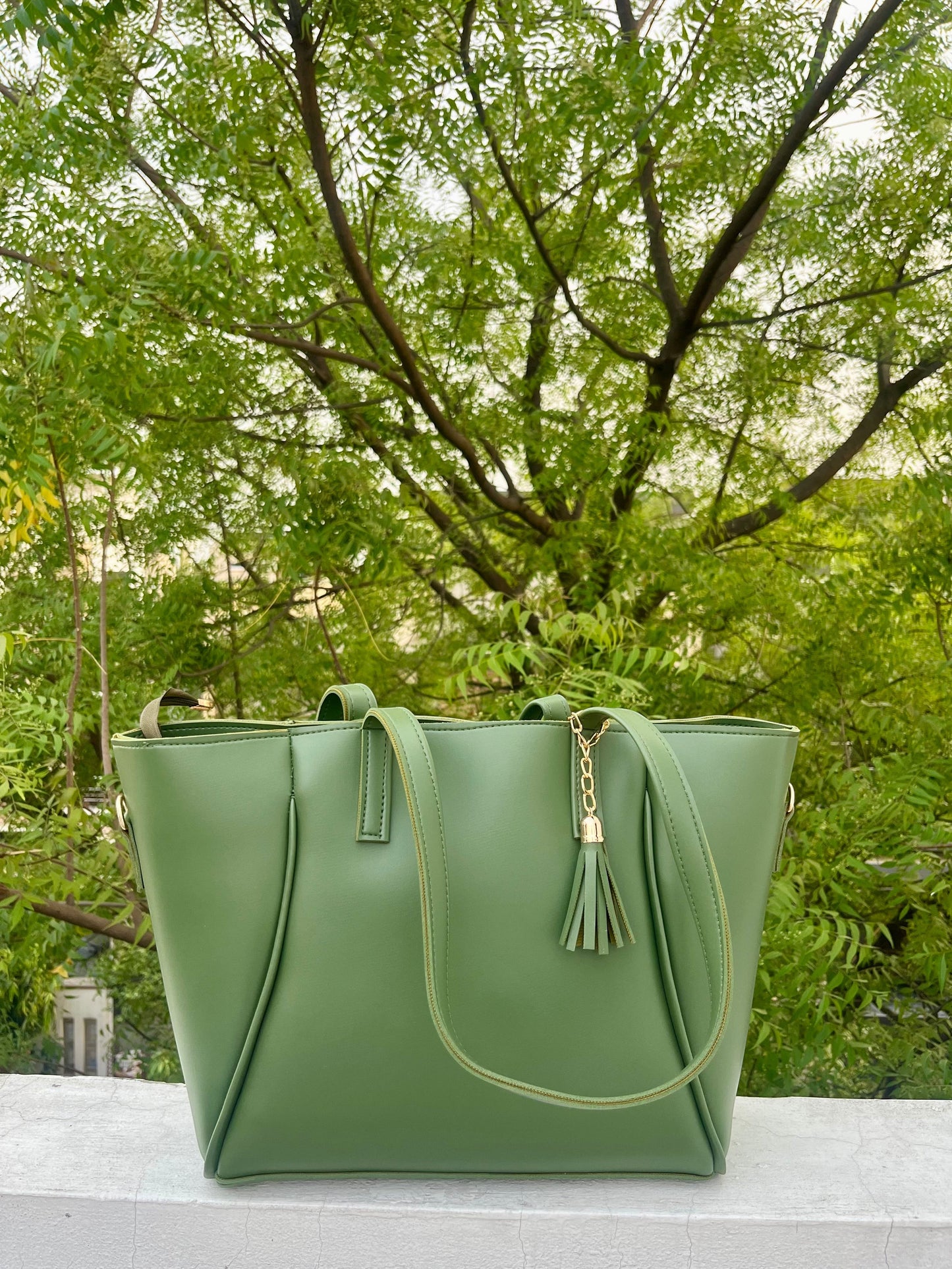 Graciza green faux leather Aura tote bag with gold-tone hardware and decorative tassel, set against a leafy backdrop.