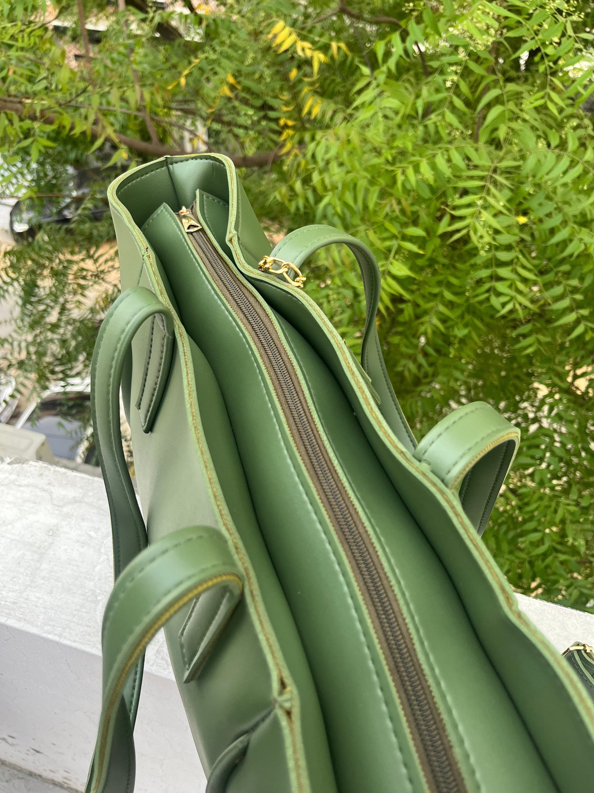 Graciza Aura green faux leather tote bag with gold-tone zipper and double handles, set against a leafy outdoor backdrop