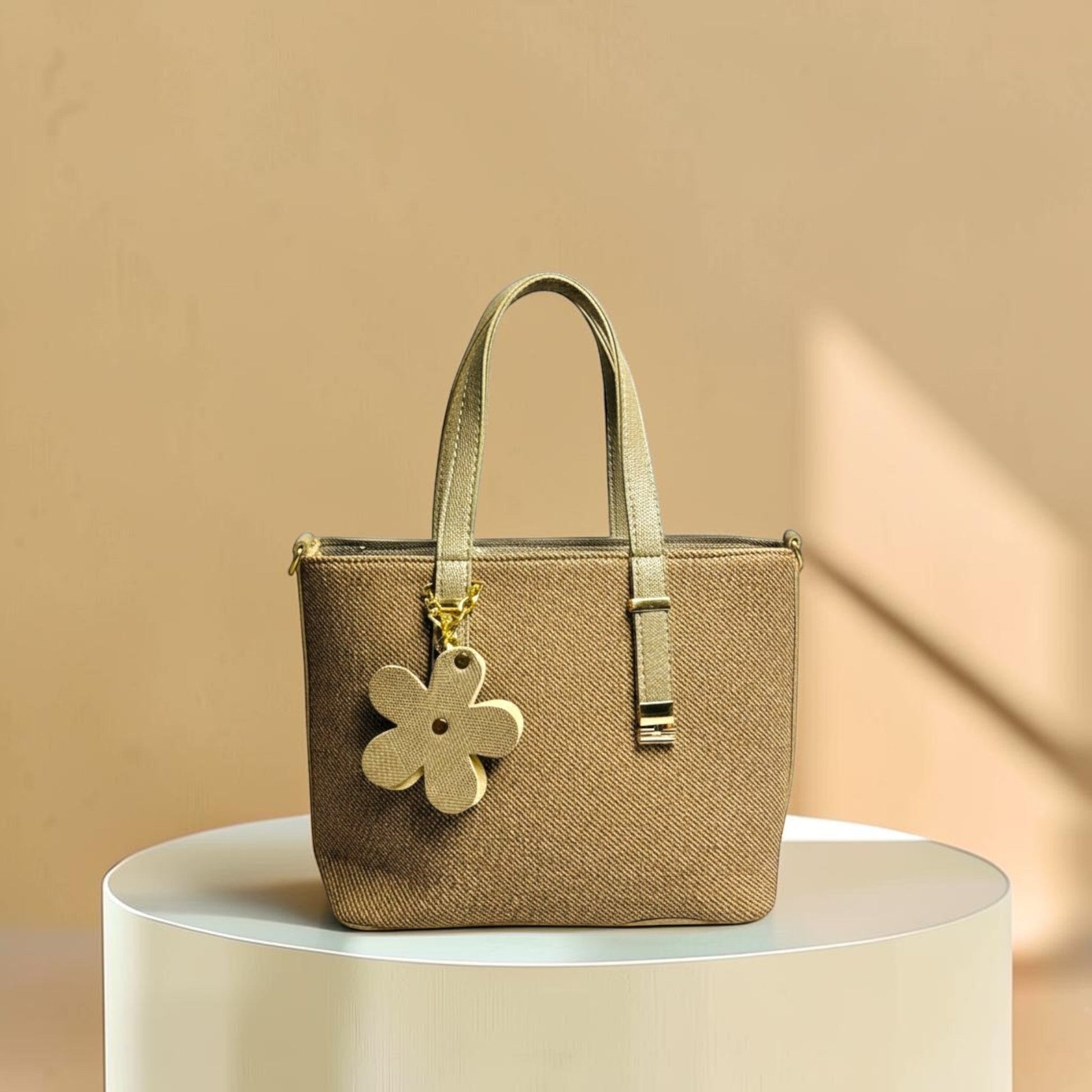Graciza Bloom beige faux leather handbag with twin handles and a decorative floral charm on a white pedestal.