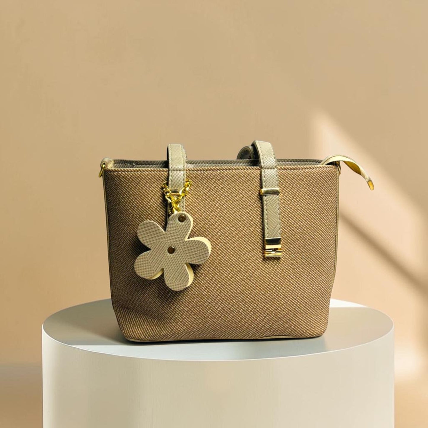 Graciza Bloom beige faux leather handbag with twin handles, adjustable strap, and a decorative floral charm.