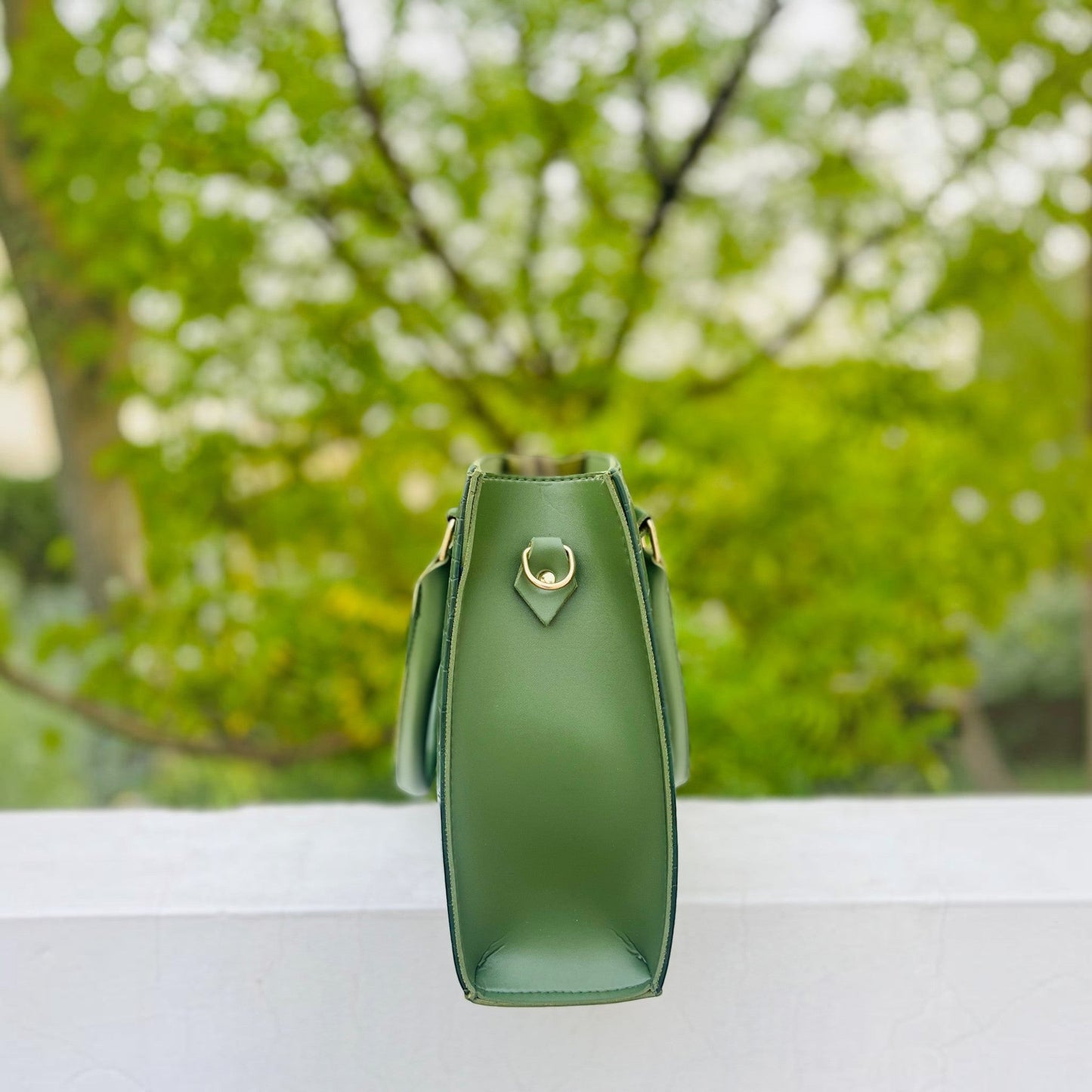 Graciza Lyra green faux leather handbag with gold-tone hardware, side view showing structured design outdoors.