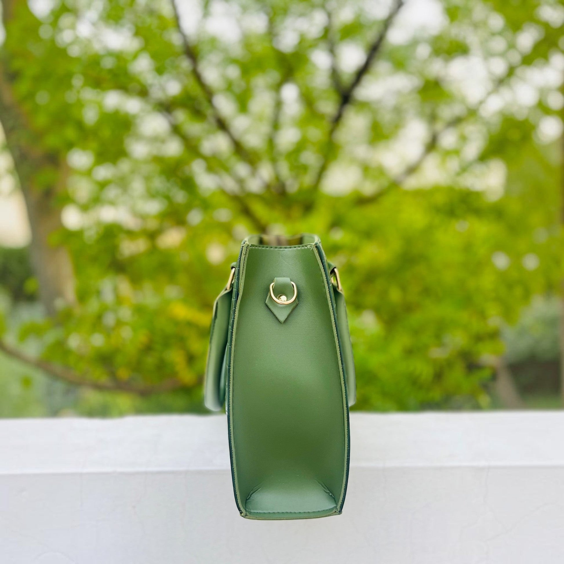 Graciza Lyra green faux leather handbag with gold-tone hardware, side view showing structured design outdoors.